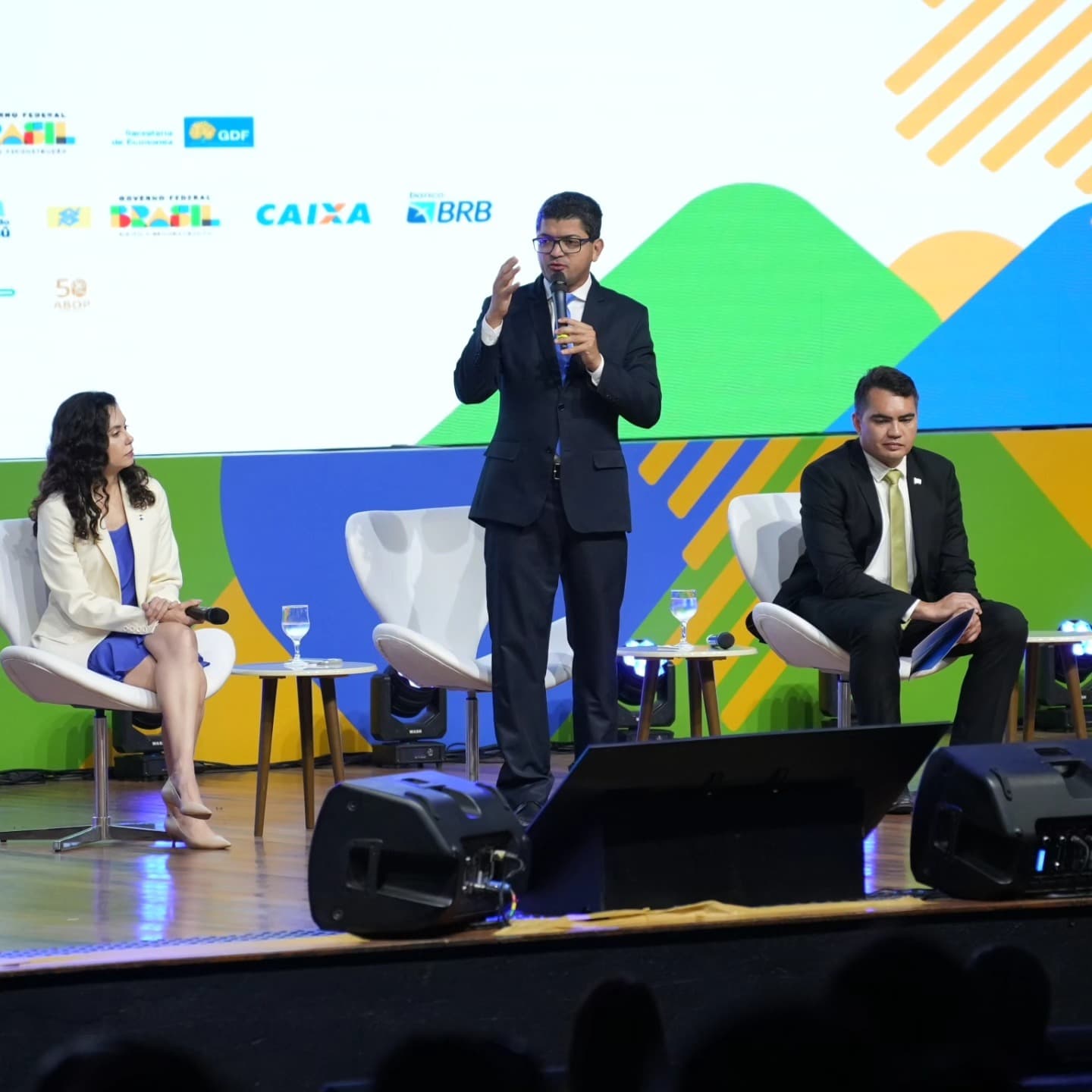 Painel de debate no palco, com painel de LED de fundo e monitores de palco.