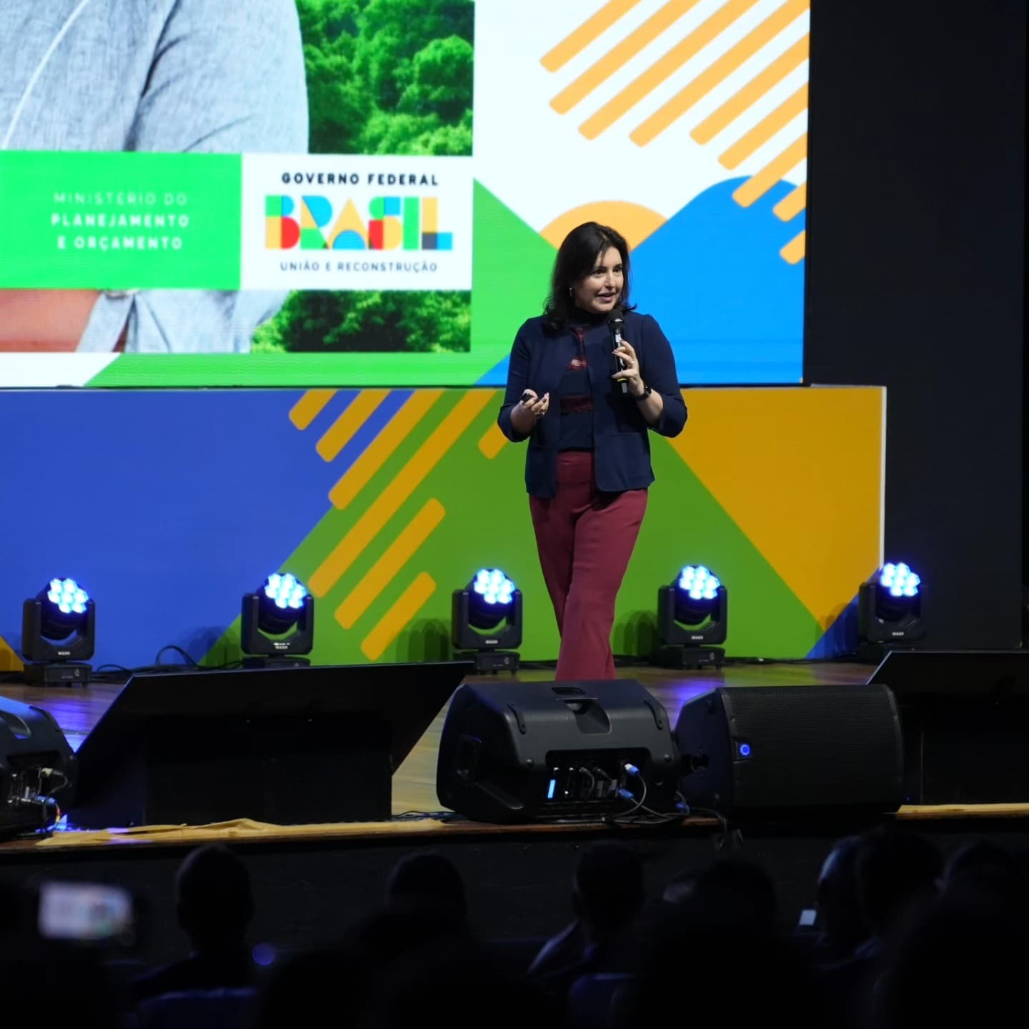 Palestrante no palco com painel de LED e sonorização de plenária.