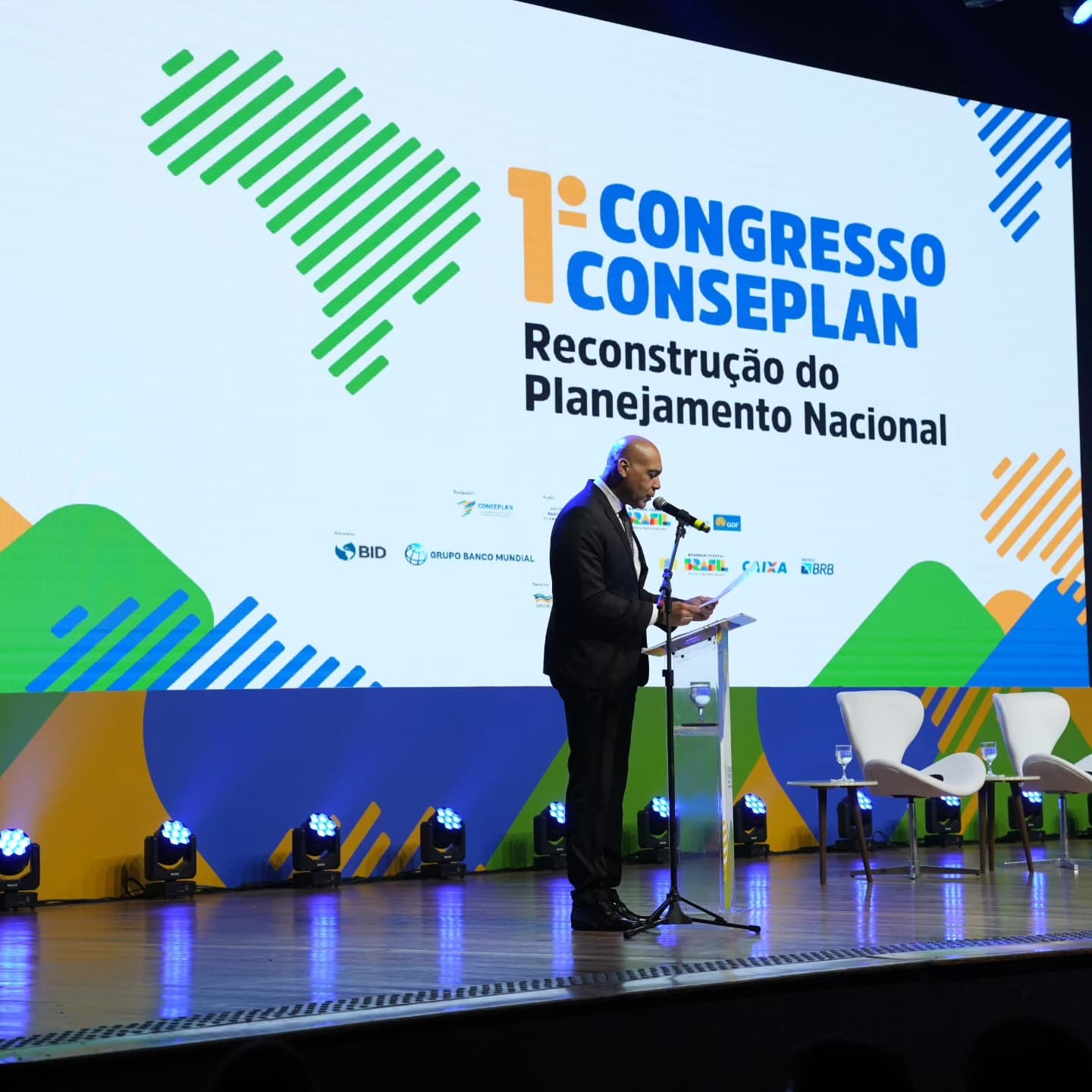 Plenária com palco amplo, painel de LED de fundo e iluminação de palco.
